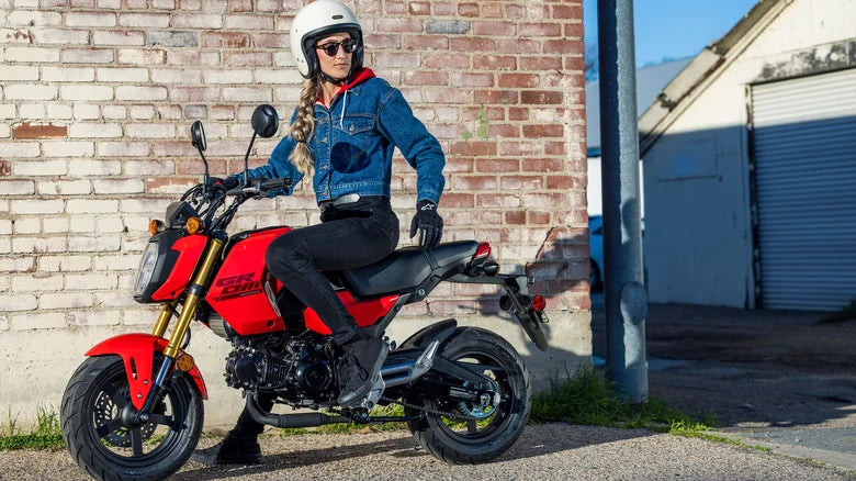 A woman posing with a red Honda Grom motorcycle, showcasing the stylish and compact design of the bike.