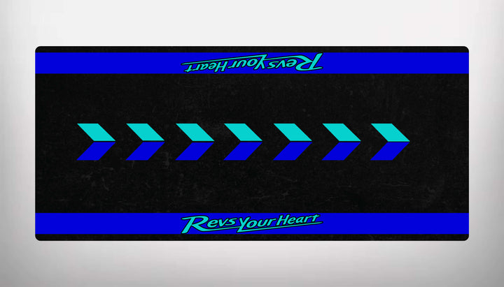 The Yamaha Universal Motorcycle Mat by Motorcycle Pit Mat is a sleek black rectangle with blue rightward arrows in the center, blue stripes at the top and bottom, and Revs Your Heart in green and teal, resembling a motorcycle floor mat design.