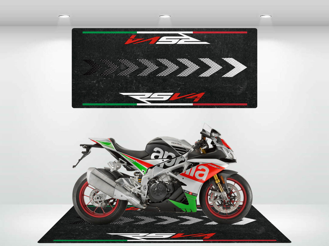 An Aprilia racing motorcycle, featuring red, green, and black colors, is displayed on a Motorcycle Mat for RSV4 by Motorcycle Pit Mat. The backdrop has arrow graphics and RSV4 text, all illuminated under bright lighting.