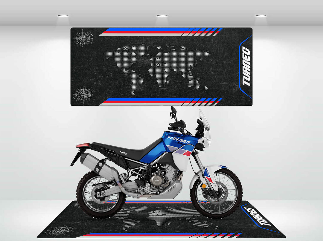 A blue and white adventure motorcycle sits on a Motorcycle Pit Mat, enhancing its striking presence. Behind it, a gray world map backdrop with red and blue accents boldly displays Tuareg, crafting an adventurous ambiance for any motorcycle garage enthusiast.