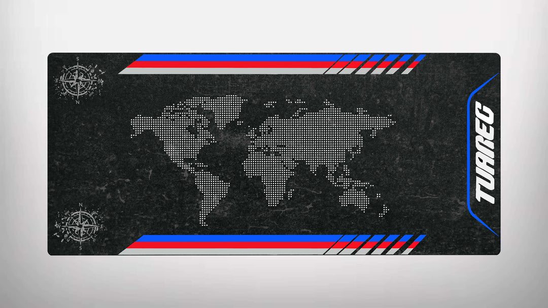 A rectangular motorcycle mat by Motorcycle Pit Mat features a world map of white dots on textured black, resembling a stylish garage mat. Compass rose symbols adorn opposite corners, while red, white, and blue stripes run along the top and bottom with TUAREG on the right side.