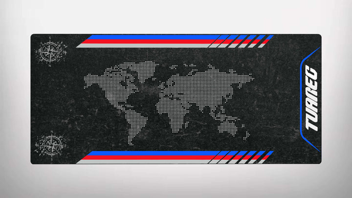 A rectangular motorcycle mat by Motorcycle Pit Mat features a world map of white dots on textured black, resembling a stylish garage mat. Compass rose symbols adorn opposite corners, while red, white, and blue stripes run along the top and bottom with TUAREG on the right side.