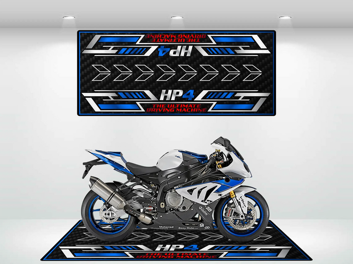 A sleek, modern motorcycle with blue and silver accents sits on the Motorcycle Pit Mats Motorcycle Mat for HP4 Carbon, showcasing its details against a backdrop featuring arrows and the phrase HP4 - The Ultimate Driving Machine in a well-lit setting.