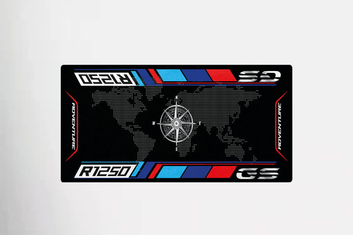 The Motorcycle Pit Mats special design features a stylized world map with a central compass rose, bordered by red, blue, and white stripes. It includes the text Adventure and R1250 GS, making it ideal for a motorcycle garage mat.