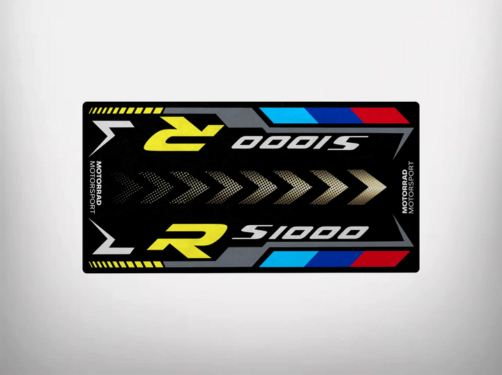 The Motorcycle Pit Mat for S1000R is a rectangular mat with S1000R in large, modern font. It features vibrant stripes of yellow, blue, red, and white. Motorsport is on the sides, complemented by dynamic arrow patterns for an enhanced sporty theme.