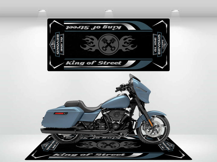 In the showroom, a stylish blue motorcycle rests on a Motorcycle Pit Mat for King of Street - Glide Beyond Limits, with a decorative panel featuring crossed wrenches and flames alongside the bold text King of Street in black and gray.