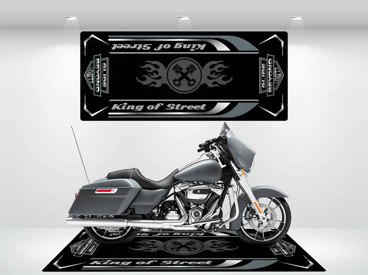 In a showroom, a sleek gray motorcycle stands on the Motorcycle Pit Mats King of Street - Glide Beyond Limits mat with flame graphics. Bright lights highlight its modern design and chrome details.