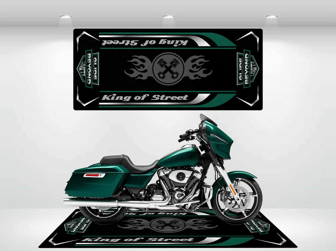 A green motorcycle is showcased on a Motorcycle Pit Mat with the bold King of Street - Glide Beyond Limits design featuring flames and crossed wrenches, alongside a matching panel above. The well-lit showroom highlights the bike as the star attraction.