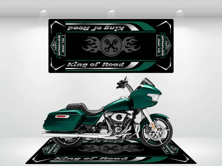 A green touring motorcycle is showcased in a showroom on a Motorcycle Pit Mat. The Harley Davidson mat and backdrop display Road Glide with flame designs in black, green, and white. Bright lighting emphasizes the sleek design and durability.