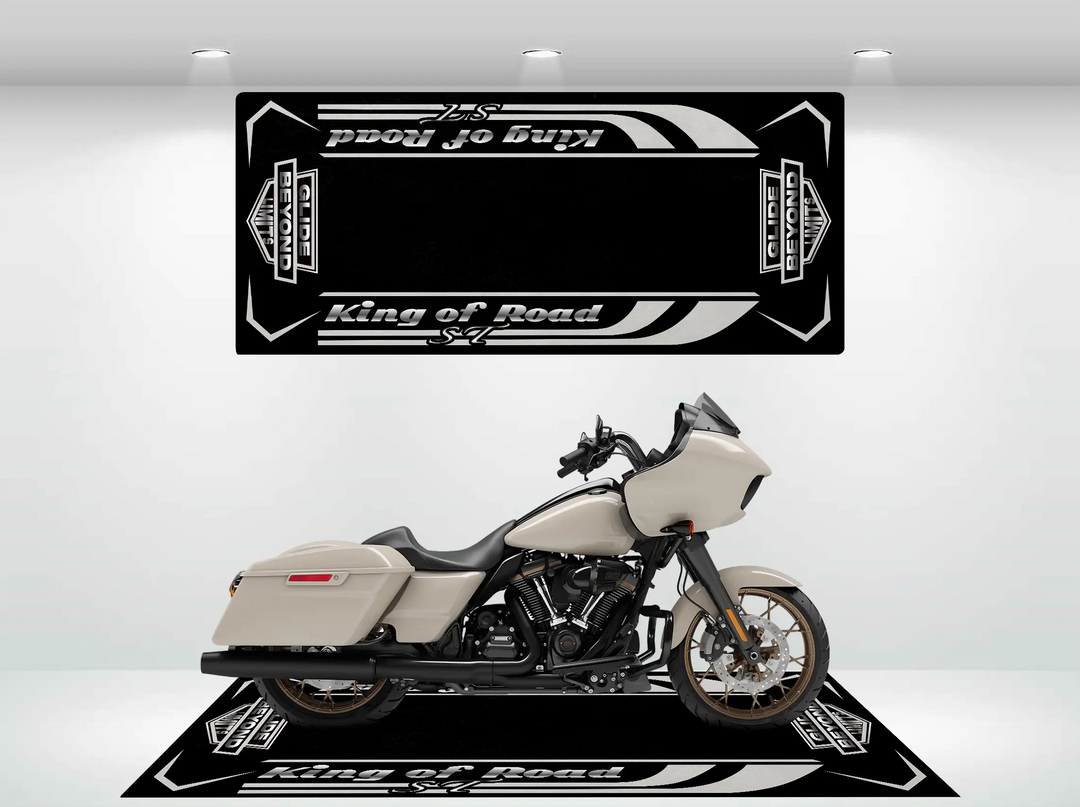 A beige Harley Davidson with a sleek design is parked indoors against a backdrop featuring Road Glide surrounded by black banners with white accents. It rests on a Motorcycle Pit Mats durable Motorcycle Mat for Road Glide ST, illuminated by spotlights above.