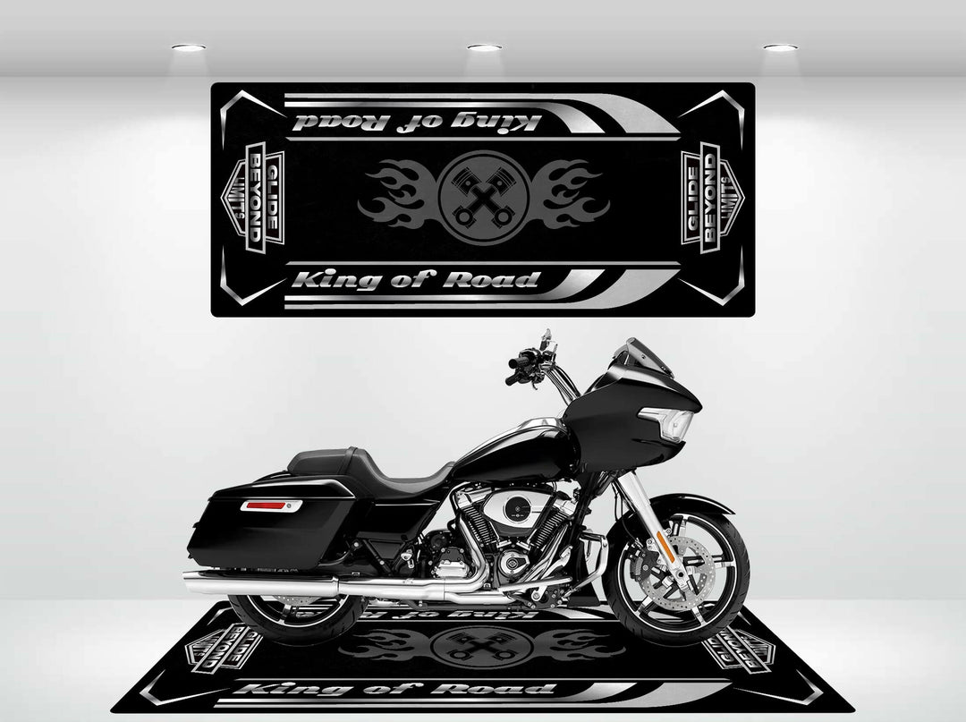 Indoors, a black motorcycle sits against vintage car logos and Proud to Play Road Glide. A durable Motorcycle Pit Mat enhances the setup. The well-lit setting highlights the bikes sleek design, with coordinating floor graphics completing the look.