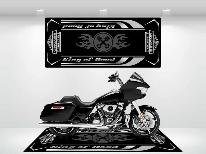 Indoors, a black motorcycle sits against vintage car logos and Proud to Play Road Glide. A durable Motorcycle Pit Mat enhances the setup. The well-lit setting highlights the bikes sleek design, with coordinating floor graphics completing the look.