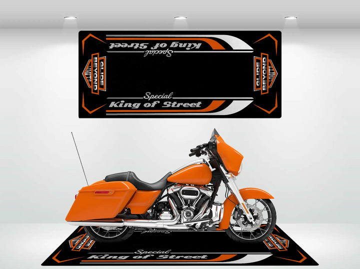 An eye-catching orange Harley Davidson is showcased indoors on the Street Glide Special motorcycle mat by Motorcycle Pit Mat. The black and orange design, with bold lettering and patterns, stands out against the white walls and bright lighting, enhancing its durability in a modern display.