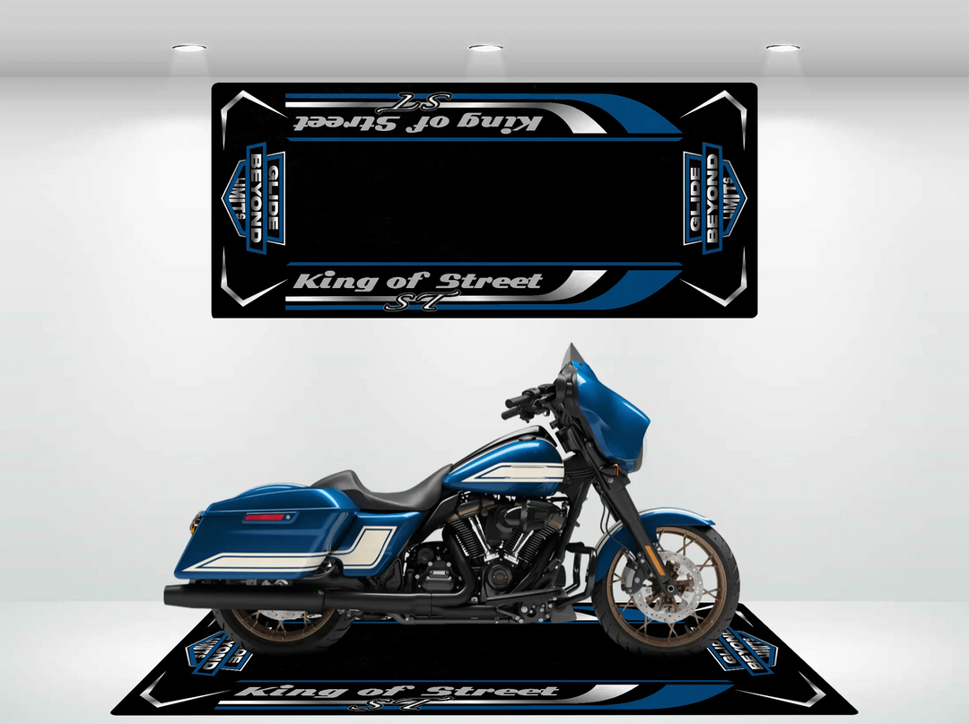 A blue motorcycle with saddlebags is displayed on a sturdy black platform featuring white and blue stripes, resembling a Motorcycle Pit Mat. The platform is branded Street Glide, with matching graphics on the wall complementing the bikes sleek design.