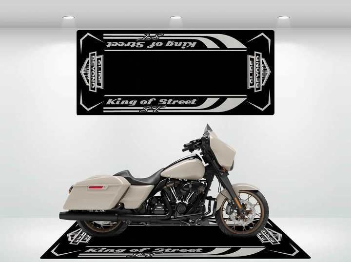 A white motorcycle with a black engine and brown wheels is parked on a Street Glide ST Motorcycle Pit Mat. The bright lighting in the white room highlights the bikes sleek design against the mats bold patterns.