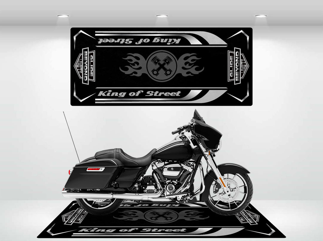 In the showroom, a sleek black motorcycle is showcased on a Motorcycle Pit Mat featuring the Street Glide design. Striking wall art with flames and crossed wrenches enhances its allure, while white background lights highlight its durability.