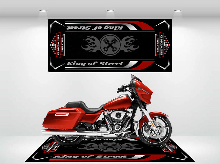 A red Harley Davidson sits on a black and red Motorcycle Pit Mat for Street Glide in a well-lit showroom, featuring text King of Street with wrenches and flames, symbolizing durability. A matching banner with the same design hangs above on the wall.