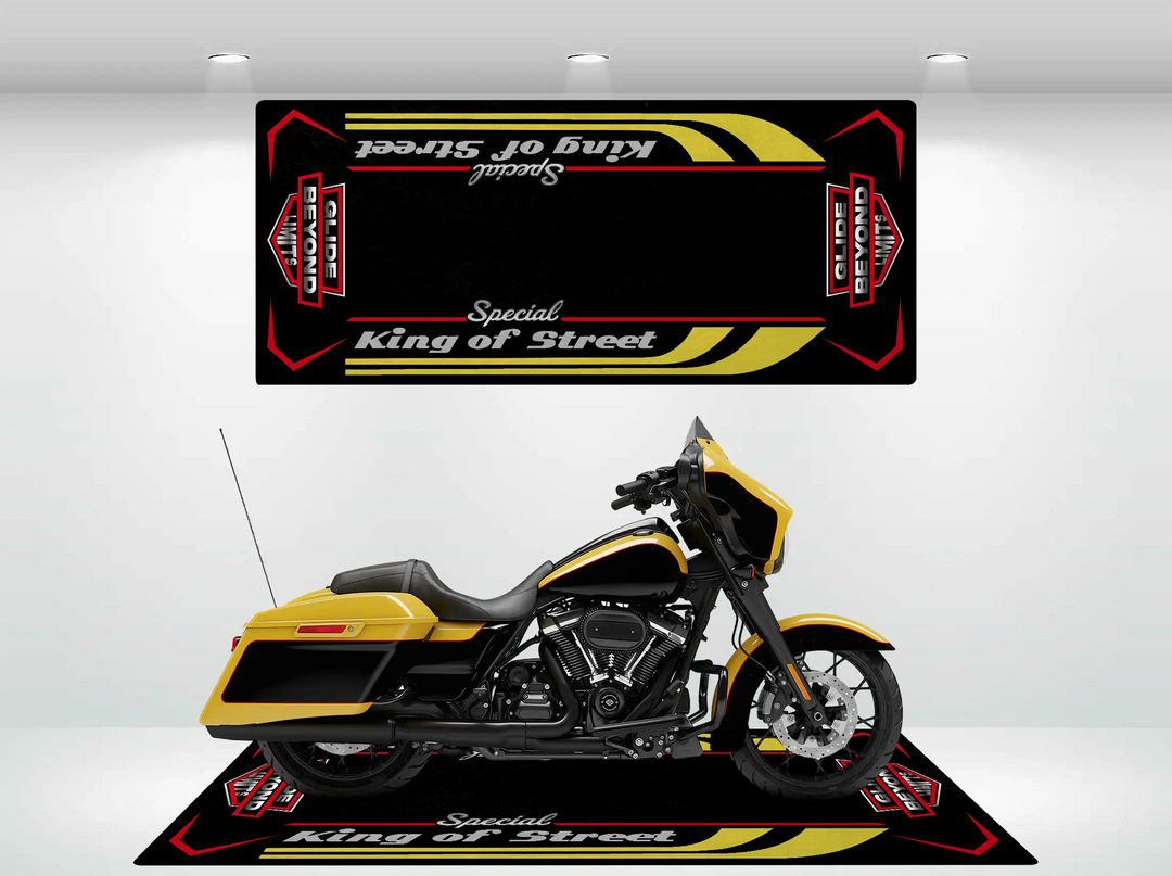 A Harley Davidson displayed on a durable black Motorcycle Pit Mat with Street Glide Special text. Above, a matching black banner with yellow and red accents hangs showing the same words, all brightly lit by overhead lighting.