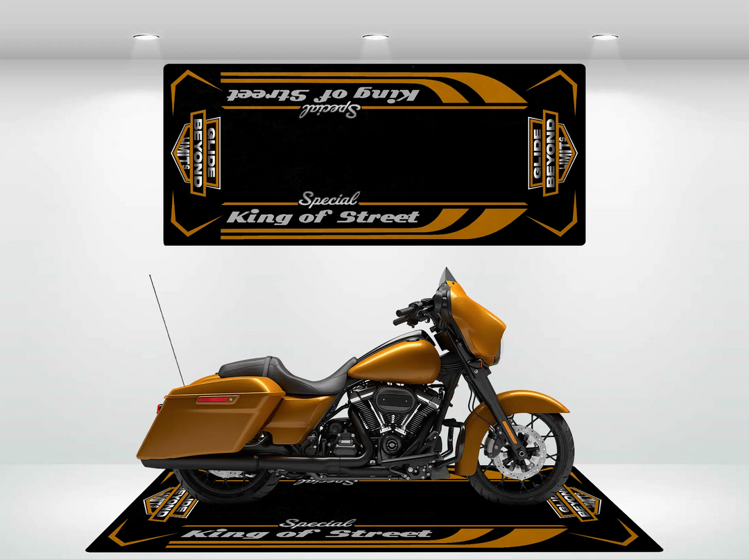 A sleek golden motorcycle is showcased on a durable black Motorcycle Pit Mat, featuring orange and white accents and labeled Motorcycle Mat for Street Glide Special. A matching banner hangs above in the well-lit Harley Davidson showroom, creating an inviting atmosphere for enthusiasts.