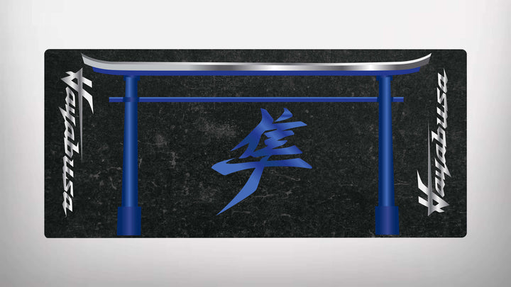 The Motorcycle Pit Mat for Suzuki Hayabusa is a black rectangular mat adorned with a blue stylized torii gate and center kanji. Vertical texts on the sides offer a symmetrical design, perfect for adding a unique aesthetic to any motorbike garage.