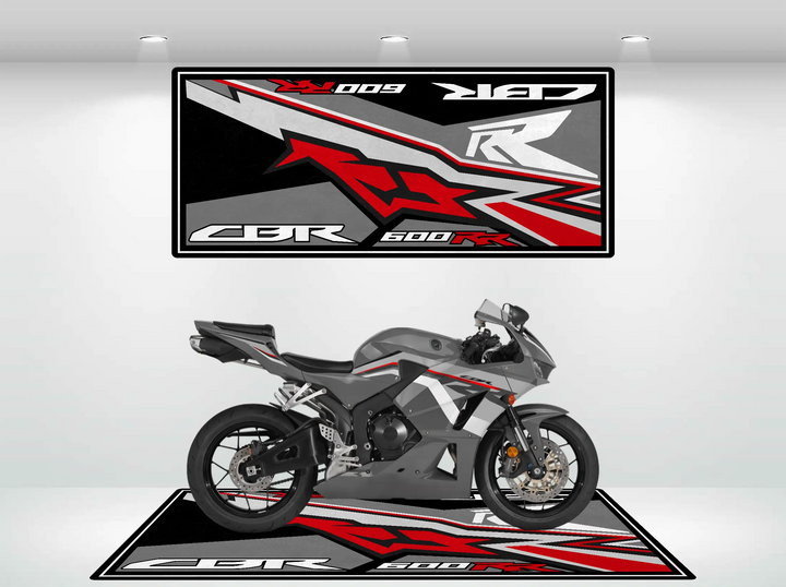 A sleek gray and red Honda CBR600RR sports motorcycle sits indoors on a Motorcycle Pit Mat, matching the bold angular wall and floor designs. The well-lit setting showcases dynamic features, making it a perfect gift choice for motorcycle enthusiasts.