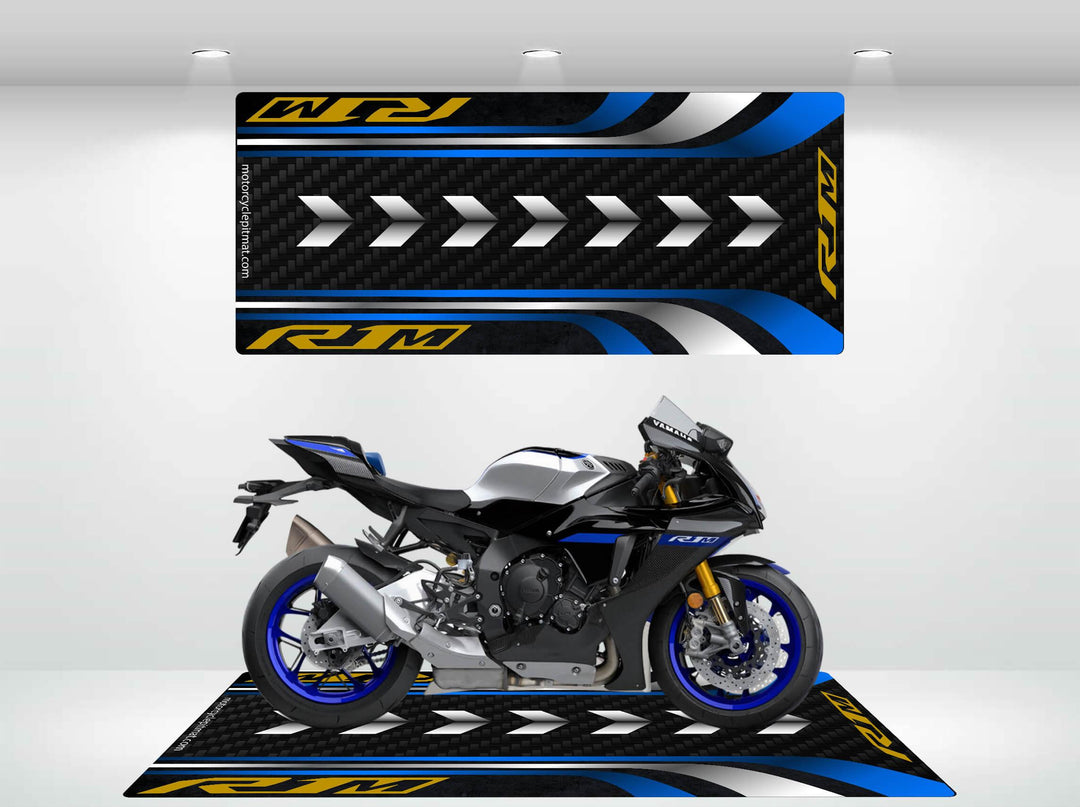 The Motorcycle Pit Mat X JDL MOTO Yamaha R1M Mat showcases a sleek black and blue motorcycle indoors, featuring matching graphics. It rests on the stylish mat adorned with arrow patterns and RJM in yellow, creating a well-lit modern racing theme ideal for avid enthusiasts.