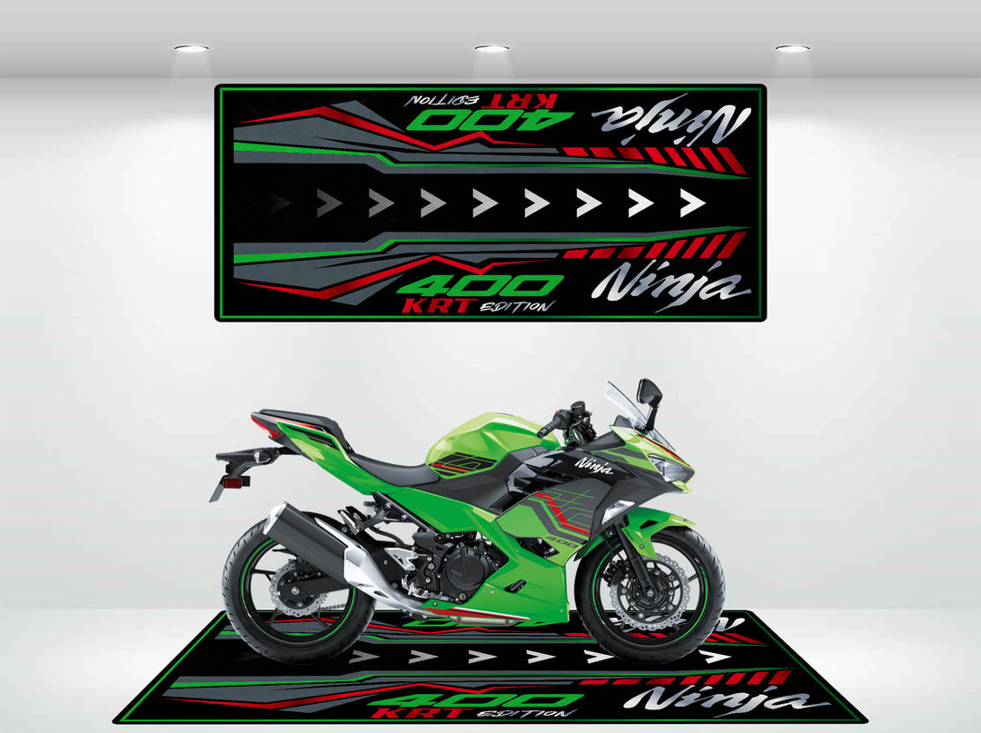 A green sport motorcycle rests on a vibrant Motorcycle Pit Mat for Kawasaki Ninja 400 KRT Edition in black, red, and green. The mat features Ninja and 400 KRT Edition, mirroring the bikes graphics against a clean white wall backdrop.