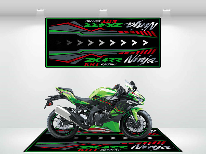 A green sport motorcycle is showcased in a showroom, placed on a Motorcycle Mat for Kawasaki Ninja ZX-4RR KRT Edition with red, black, and green geometric designs. Above, a matching wall mat mirrors the floors aesthetic and features the words Ninja and KRT Edition.