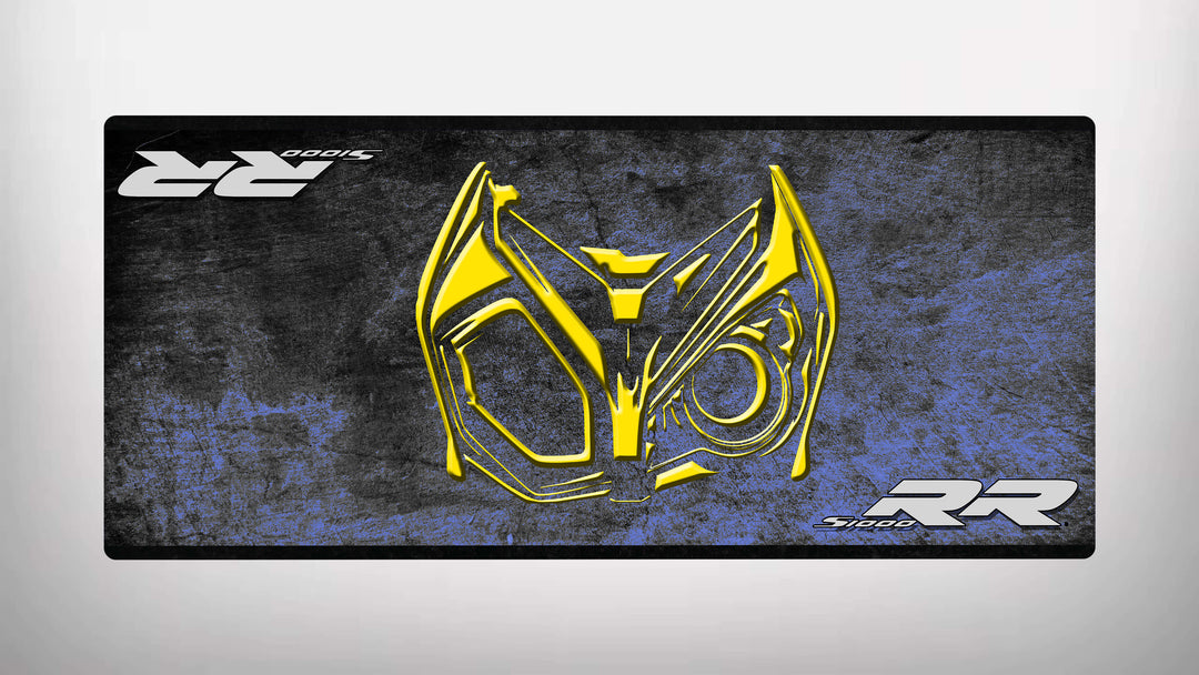 A digital artwork displays a stylized yellow animal-like face with bold eyes and angular lines against a textured dark blue and black backdrop. The design is reminiscent of the Motorcycle Pit Mat for the S1000RR, featuring RR and SIODOS in opposite corners.