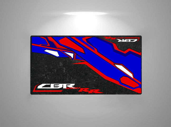 The Motorcycle Pit Mat for Honda CBR1000RR features a vibrant design with bold red, blue, and white angular graphics. Displaying CBR and RR, the rectangular mat enhances any space with its dynamic motorcycle-inspired flair on a dark background.