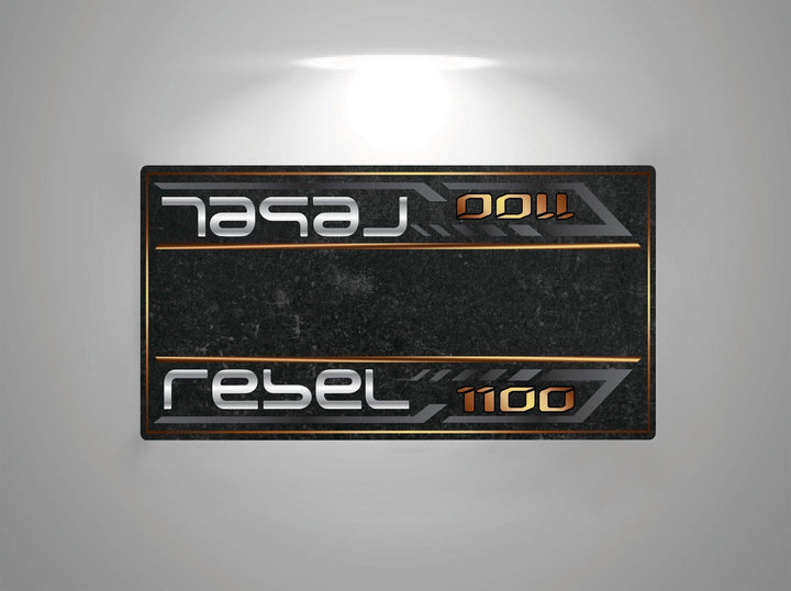 The Motorcycle Pit Mat for Honda Rebel 1100 is a metallic, rectangular sign with a dark textured surface and rebel 1100 written in futuristic silver and orange. The text mirrors at the top, with a soft glow from a light source above.