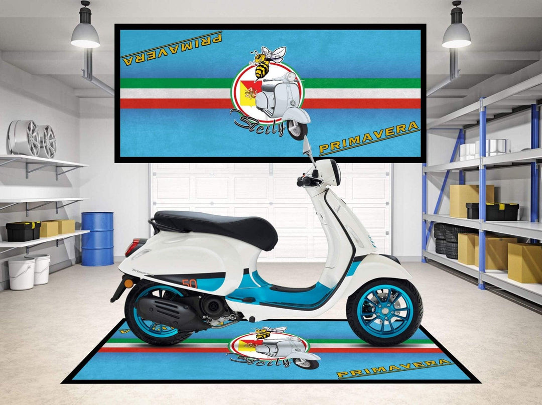 A white and blue scooter sits on a Motorcycle Pit Mat in a garage with shelves and a gray door. A large wall rectangle displays a bee riding a scooter, featuring Vespa and Primavera in bold red and blue against striped background.