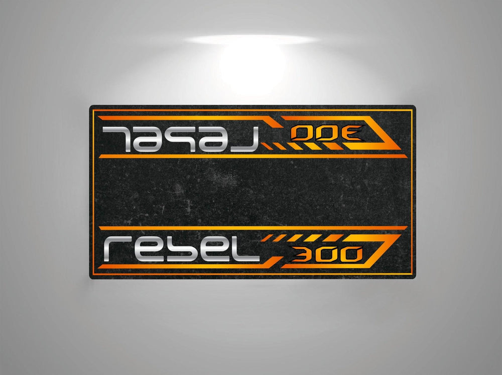 The Motorcycle Pit Mat for the Honda Rebel 300 features a rectangular label with rebel 300 in futuristic silver font on a dark background. Orange lines and arrows accentuate the symmetrical design, with flipped text on both halves, making it a striking addition to any motorcycle floor setup.