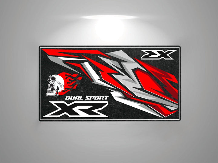 The Motorcycle Pit Mat for Honda XR showcases an abstract design with sharp red, gray, and black shapes and a stylized skull with flames. The text DUAL SPORT XR and XX stands boldly on the dark background, capturing the allure of a motorcycle garage mat.