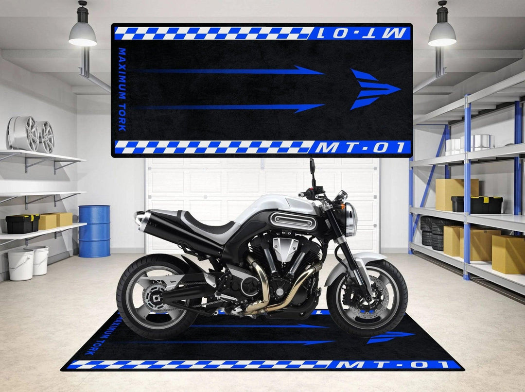 A modern garage showcases a sleek motorcycle on a Motorcycle Pit Mat for Yamaha MT-01, featuring a blue and black arrow design with MT-01 and MAXIMUM TORK. Well-lit shelves holding car parts and tools ensure the space is organized.