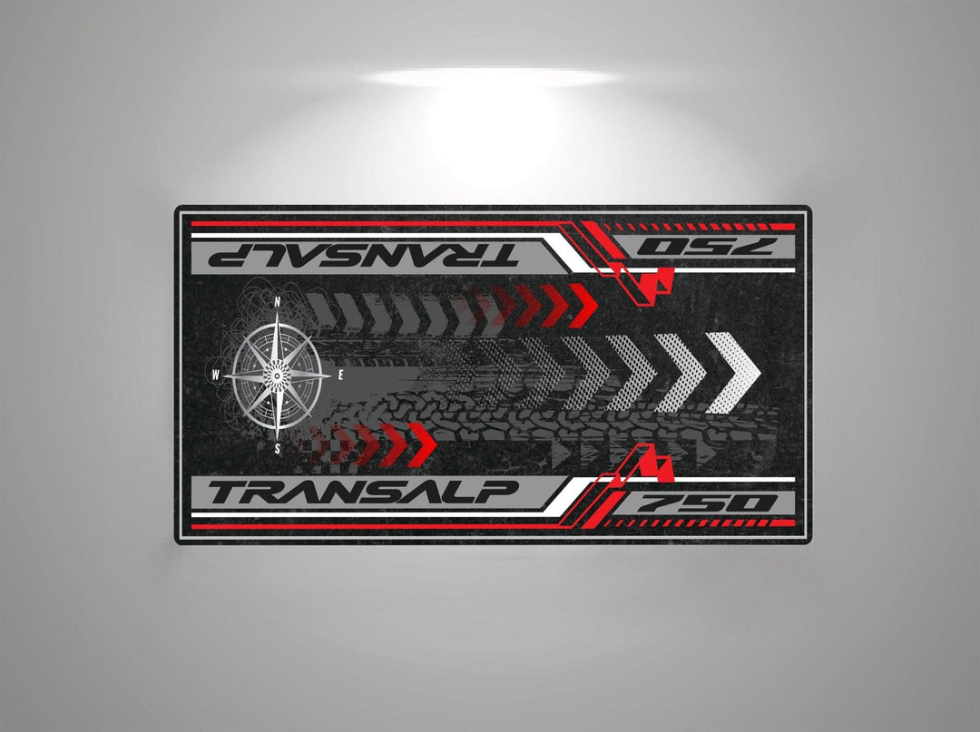 The Motorcycle Pit Mat for the Honda Transalp 750 features a racing-themed design with Transalp and 750, red and white stripes, arrows, a compass motif on a dark background, and tire tread patterns.