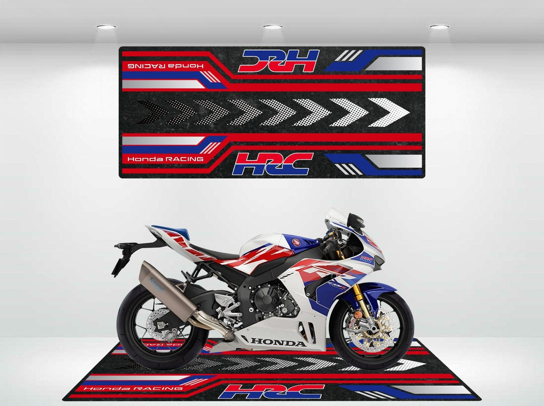 In the showroom, a Honda racing motorcycle stands on a vibrant Motorcycle Pit Mat for Honda HRC, featuring a striking white, red, and blue design. Behind it hangs a matching wall banner with the iconic HRC logo and arrows and stripes that echo the bikes colors.