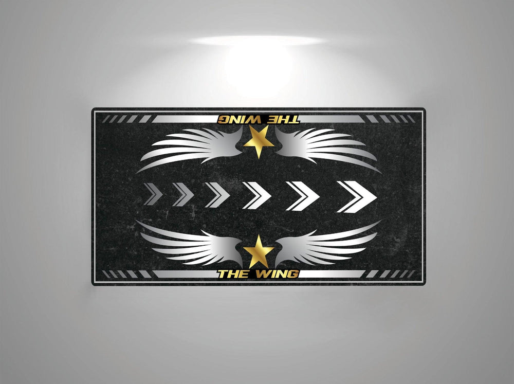 The Motorcycle Pit Mat features a rectangular design with THE WING at the top and bottom, white wings, right-pointing arrows, and yellow stars on a dark textured background, reminiscent of a motorcycle mat for Honda Goldwing under overhead light.