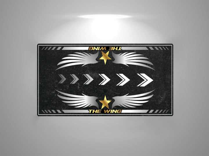 The Motorcycle Pit Mat features a rectangular design with THE WING at the top and bottom, white wings, right-pointing arrows, and yellow stars on a dark textured background, reminiscent of a motorcycle mat for Honda Goldwing under overhead light.