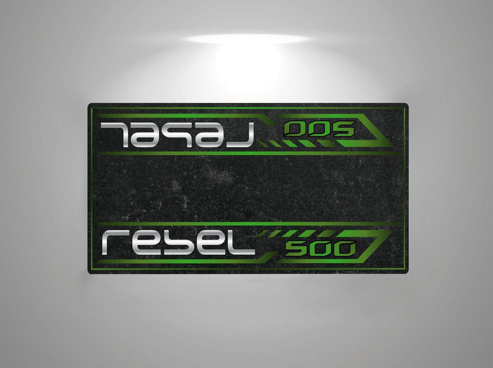 A rectangular sign resembling a Motorcycle Pit Mat for Honda Rebel 500 displays 500 in green and rebel in white, styled with a metallic and industrial motorbike mat look. The dark background features a subtle green and black pattern.