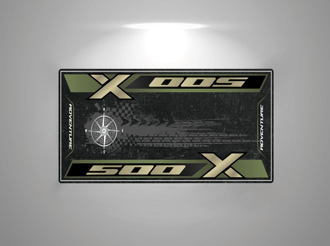 Image of a rectangular banner with Motorcycle Mat for Honda CB500X and 500 X against a green and black background, featuring tire tread design and compass graphic, resembling a Motorcycle Pit Mat; ADVENTURE is vertically on both sides.