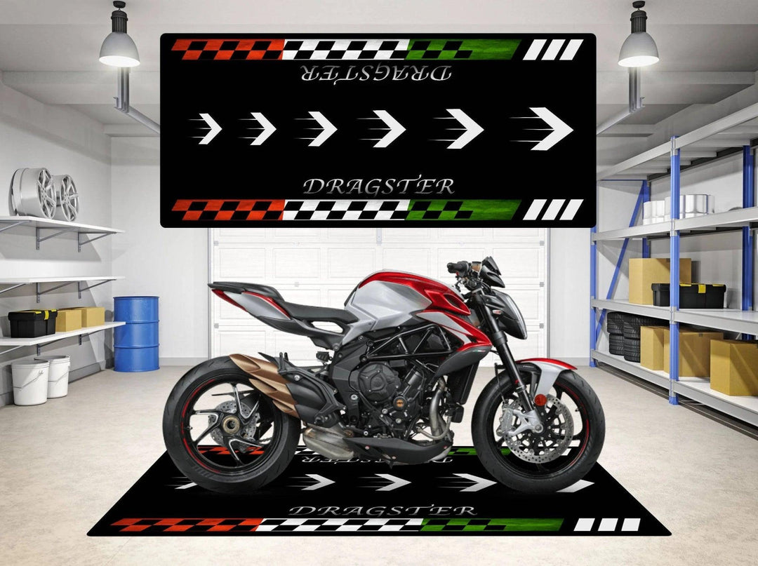 A red and silver motorcycle sits on a Motorcycle Pit Mat for MV Agusta Dragster in a garage, alongside a matching wall banner featuring the word Dragster with arrow designs in black, green, red, and white. Shelves and storage items are visible in the background.