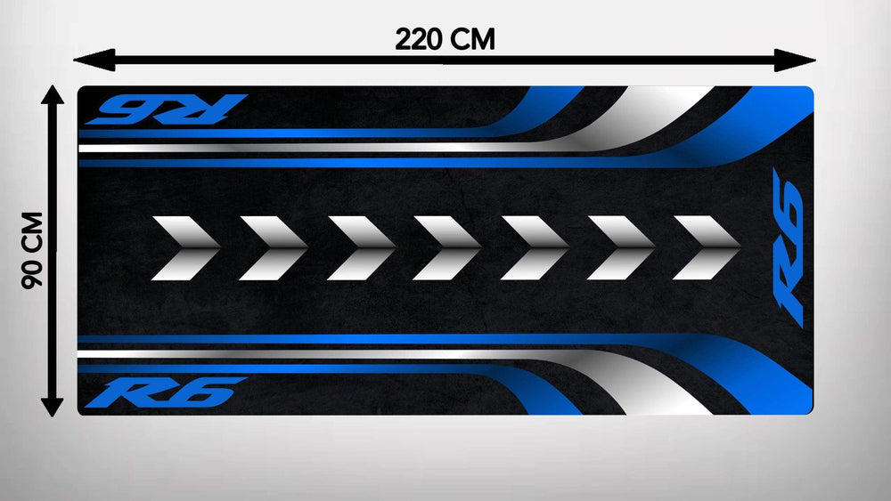 The Motorcycle Pit Mat for Yamaha R6 is a rectangular garage mat measuring 220 cm by 90 cm with a black background, blue and white stripes on the edges, white arrows pointing right in the center, and R6 written in blue on both ends.