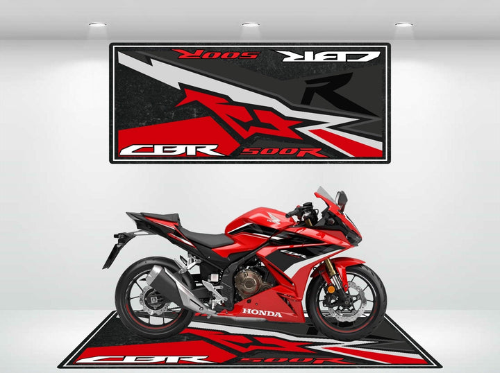 In a showroom, a red sports motorcycle rests on a Motorcycle Pit Mat designed for the Honda CBR500R, while an overhead poster with bold graphics displays CBR 500R, enhancing the bikes sleek design in the well-lit setting.