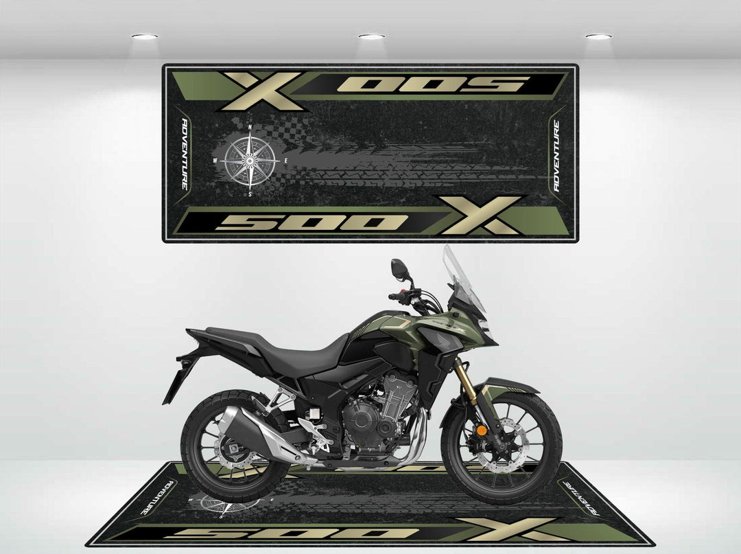 In a showroom, a green sport motorcycle stands proudly on a Motorcycle Pit Mat designed for the Honda CB500X, with two branded mats displaying 500X. Spotlights on the wall elegantly illuminate the setup.