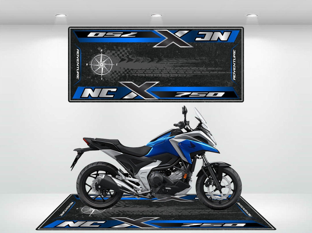 A blue and black motorcycle sits on a Motorcycle Pit Mat featuring white tire tracks and adorned with NC 750X and geometric designs in blue and white. The scene is set indoors with spotlighting highlighting the Motorcycle Mat for Honda NC750X.