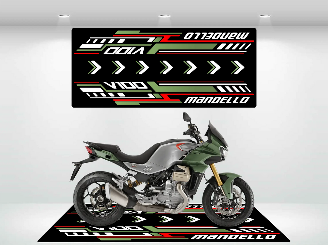 A sleek green motorcycle in a modern showroom rests on a Motorcycle Pit Mat featuring bold red, green, and white geometric designs. Mandello and V100 are showcased in striking lettering, all bathed in bright spotlights.