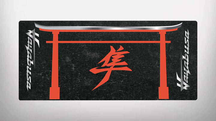 The Motorcycle Pit Mat for Suzuki Hayabusa is a black rectangular mat featuring a red torii gate with a prominent red kanji character in the center. Sleek white and silver alphanumeric symbols run vertically along the sides, capturing the essence of motorbike culture.