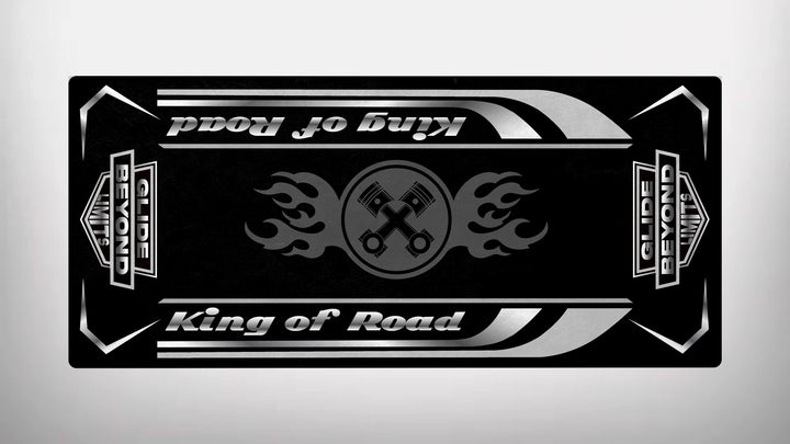 The Motorcycle Pit Mats Motorcycle Mat for King of Road - Glide Beyond Limits features a black and silver design with King of Road, stylized flames, crossed wrenches at the center, and the phrase Glide Beyond Limits on the sides within a rectangular border.