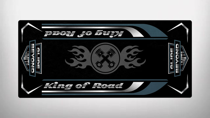 A rectangular graphic on a black Motorcycle Pit Mat features King of Road twice in white, two silver keys with flames at the center, and Glide Beyond Limits on dark corners with light accents, ideal for your motorcycle garage setup.